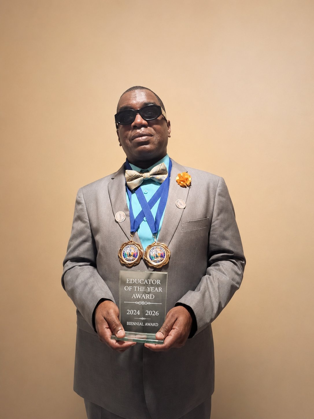 Kevin E. Cartwright wearing a grey suit and bow tie, holding the Disability Icon Educator of the Year Award recognizing his achievements in 2024 and 2026.